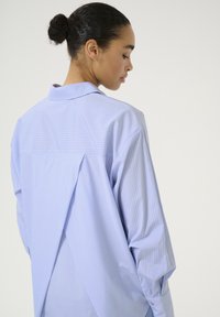 Camicia a righe blu chiaro con vestibilità rilassata, dotata di dettaglio a spacco sul retro, colletto a punta e polsini con bottone. Tessuto leggero e morbido.
