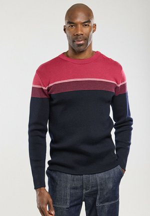 Pull en tricot avec un corps bleu marine et une partie supérieure rouge. Présente des rayures blanches horizontales et des accents de boutons à l'épaule. Texture douce.