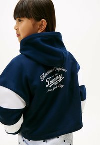 Granatowy hoodie z białymi akcentami, z wysokim kołnierzem i graficznym logo na plecach. Miękka tkanina z luźnym krojem.