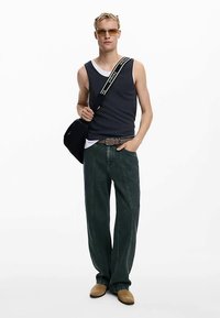 Musta toppi valkoisen paidan päällä, rentoistuvaiset tummanvihreät farkut, vaaleanruskeat slip-on-kengät ja pieni musta olkalaukku, jossa on logolla varustettu hihna.