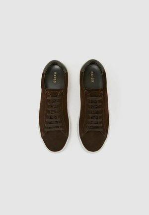 Hnědé semišové tenisky s hladkou černou koženou patní částí, šněrování a bílou gumovou podrážkou. Logo vytištěné uvnitř boty.