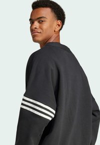 Sort sweatshirt med en afslappet pasform, ribbet halsudskæring og hvide striber på ærmerne. Blødt stof med en glat tekstur.