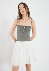 Grå stripet topp med frontknute og bølget kant, kombinert med en hvit lagdelt skjørt med strukturert stoff og et flytende design.