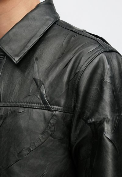 Čierna kožená bunda s textúrovaným povrchom, štandardným golierom a viditeľnými švami na pleciach a v oblasti hrudníka.