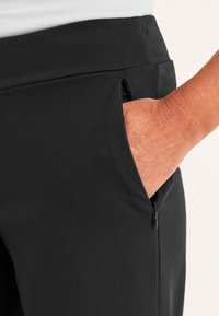 Zachte zwarte stoffen broek met een ritszak aan de zijkant, voorzien van een gladde textuur en een aansluitend ontwerp. De tailleband is breed en plat.