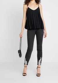 Top de tirantes finos plisado en negro, combinado con jeans ajustados negros con dobladillo deshilachado y un bolso de cuentas. Tacones negros.