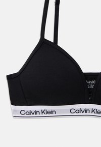 Čierny bralet z hladkej látky, s nastaviteľnými ramienkami a bielym značkovým pásom s textom "Calvin Klein" v kontrastnom dizajne.