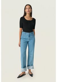 Top negro de canalé con mangas cortas, detalles de botones, combinado con vaqueros de pierna ancha azul claro, remangados en los tobillos, y zapatos slingback negros.