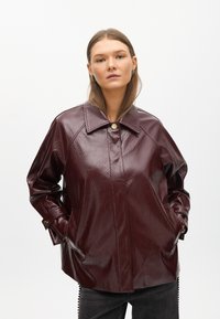 Bordová koženka so lesklým povrchom, veľký golier, bočné vrecká a zapínanie na patentky. Voľný, oversized strih.