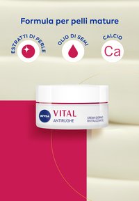 Crema idratante in un barattolo bianco con un accento rosa. Il testo include "VITAL" e "ANTI-RUGHE". Lo sfondo presenta una texture simile alla crema.