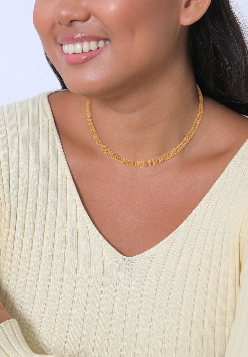 Gelbe Choker-Halskette mit einem strukturierten, gewebten Design liegt auf einem glatten Hals, kombiniert mit einem hellgelben, gerippten Pullover mit V-Ausschnitt.