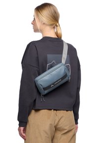 Sac à bandoulière gris au design rectangulaire élégant, fabriqué à partir d'un matériau lisse et présentant une bande d'accent noire ainsi qu'un logo.