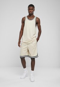 Beige ermeløs tank topp og shorts-sett med svart kant. Tøyet ser mykt og strukturert ut. Kombinert med hvite sneakers og sokker.