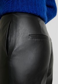 Czarne skórzane spodnie o gładkiej fakturze, z tylną kieszenią i subtelnym przeszyciem, zestawione z jasnoniebieskim swetrem z dzianiny.