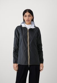 Giacca leggera nera con un interno bianco a contrasto, chiusura con zip e dettagli gialli, e cappuccio aderente. Texture liscia, maniche lunghe.