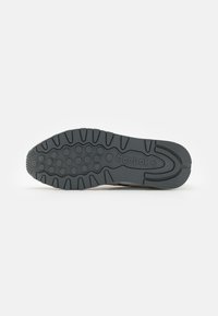 Suela de goma de una zapatilla Reebok con patrones de agarre circulares y surcos, mostrada sobre un fondo blanco liso.