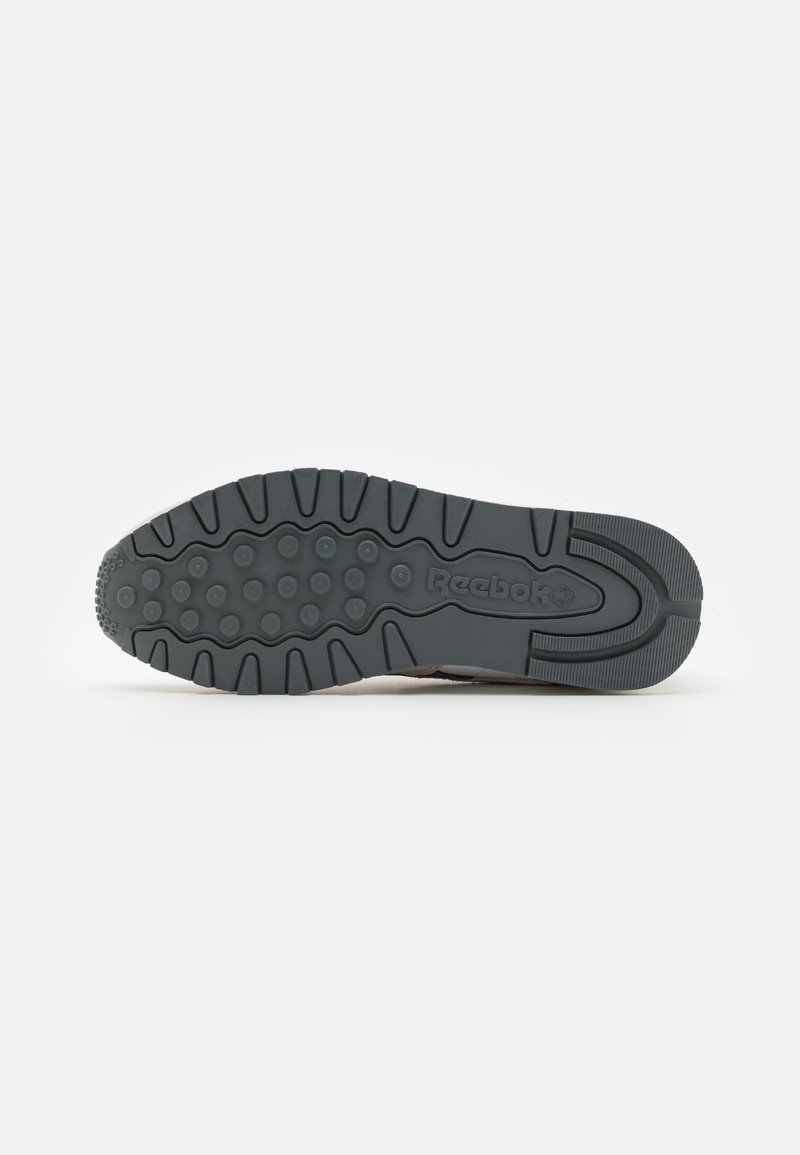 Semelle en caoutchouc d'une chaussure Reebok avec des motifs de grip circulaires et des rainures, présentée sur un fond blanc uni.