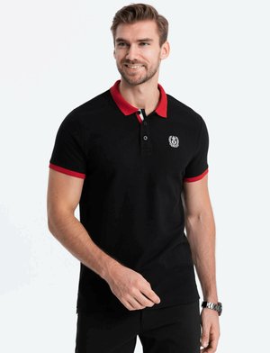 Musta polo-paita punaisella kauluksella ja yksityiskohdilla, jossa on logo rintamuksessa, lyhyet hihat ja vartalonmyötäinen muotoilu.