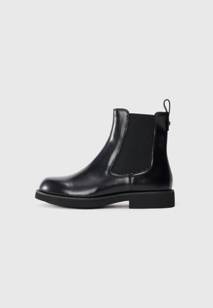 Bottine Chelsea en cuir noir avec panneau latéral élastique, tirettte au talon, semelle bloc basse, présentée sur fond blanc.