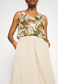 Top in tessuto verde oliva con motivo floreale e scollatura a V, abbinato a una gonna beige con bottoni frontali e tasche laterali, caratterizzata da una texture morbida e fluida.