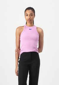 Top in cotone rosa a costine con un design aderente, scollatura alta e un piccolo logo blu. Abbinato a pantaloni neri a vita alta.