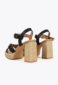 Sandalias de plataforma negras con tiras, con un tacón alto bloque tejido de color natural y parte superior de cuero suave. Incluyen correas ajustables en el tobillo.
