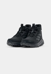 Black hiking shoes with a textured upper, reinforced toe, and three parallel stripes. Features a rugged sole for traction.