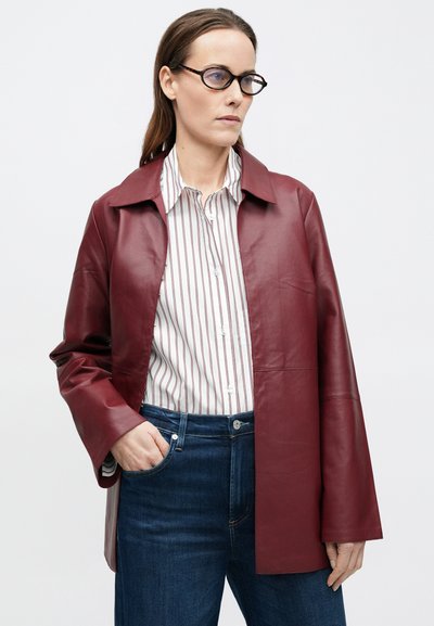 Bordó bőrdzseki klasszikus gallérral, fehér és bordó csíkos inggel, sötétkék farmerrel párosítva. Laza szabású, minimális dizájnnal.
