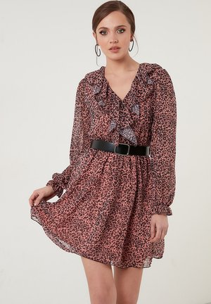 Vloeiende roze jurk met een luipaardprint, gerimpelde V-hals, lange mouwen en een zwarte riem om de taille. Doorzichtige stof voegt textuur toe.