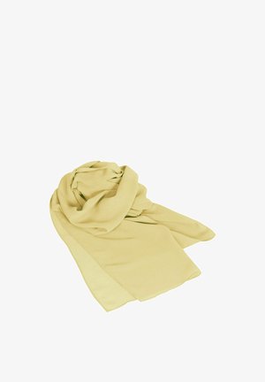 Femme debout portant une robe longue jaune pâle sans bretelles, fluide, avec une écharpe assortie autour du cou et un bracelet doré au poignet droit.