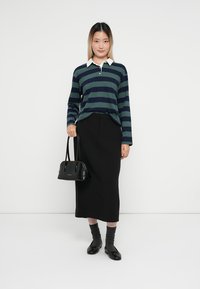 Polo cu mânecă lungă în dungi, de culoare bleumarin și verde, asociat cu o fustă creion neagră. Accesoriile includ o mică geantă de mână neagră și pantofi stilați negri.