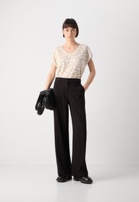 Haut en tricot beige à imprimé léopard avec un décolleté en V, associé à un pantalon large noir, tenant un sac à main texturé noir. Des bottes à semelle plate complètent le look.