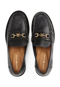 Mocassins en cuir noir avec un accent en métal doré sur le dessus, doté d'un bout arrondi et d'un design à enfiler. Intérieur doux et rembourré.
