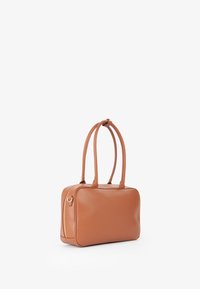 Sac en cuir tan de forme rectangulaire, avec deux longues poignées et une fermeture éclair sur le côté. Texture lisse avec des accents de matériel minimalistes.
