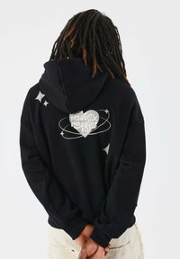 Sudadera negra con un gráfico en la espalda que presenta un diseño de corazón y el texto "Proyecto París", rodeado de estrellas y remolinos estilizados.