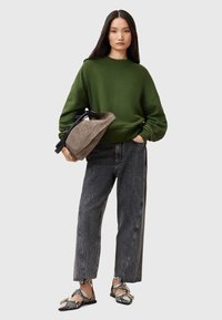 Grön oversized sweatshirt, grå högmidjade jeans och mönstrade ballerina-skor. En texturerad brun väska hålls i ena handen. Enkel, modern design.