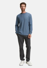 Lichtblauw shirt met lange mouwen van zachte stof, gecombineerd met donkergrijze broek. Witte sneakers maken de outfit compleet. Eenvoudig ontwerp, geen patronen.