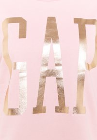 Rosa tyg med stora, glänsande guldbokstäver som stavar "GAP" i en fet, blockbokstavsfont.