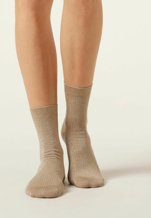 Calcetines de tobillo en tono dorado con una textura acanalada y acentos de purpurina, con un diseño de puño que se sitúa justo por encima del tobillo.