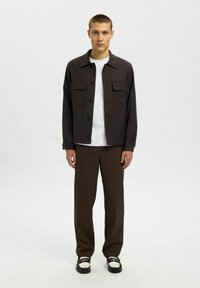 Zwarte overhemde met twee borstzakken, gecombineerd met bruine wijde broek en zwart-witte schoenen. Gladde stof met een getailleerde pasvorm.