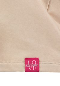 Tela beige con dobladillo cosido y una pequeña etiqueta rosa que dice "LOVE" y "KETLARGO" en texto blanco.