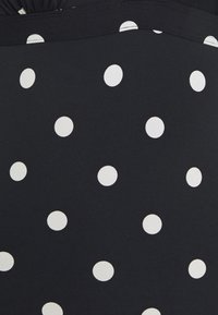 Schwarzer Stoff mit großen weißen Pünktchen, glatte Textur, mit einem gerafften Detail an der Oberseite.