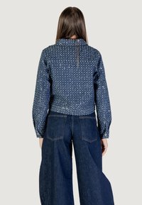 Giacca di jeans cropped con paillettes luccicanti, maniche lunghe e colletto. Indossata con jeans a gamba larga in denim scuro, dotati di tasche posteriori.
