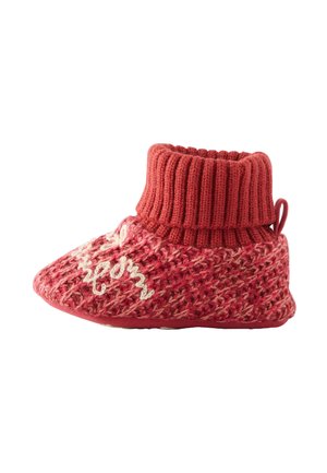 Roter gestrickter Hausschuh mit einem gerippten Bund, texturiertem Körper und weißem gesticktem Detail. Besitzt eine abgerundete Zehenpartie und eine flexible, strukturierte Sohle.