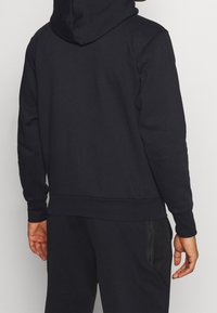 Sweat à capuche en tissu bleu marine foncé. Présente une coupe décontractée, des poignets et un ourlet côtelés. Comprend des accents sur les panneaux latéraux avec un détail texturé.