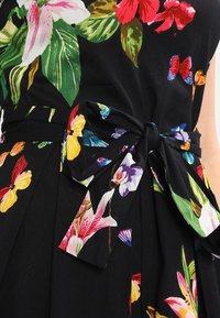 Czarna tkanina z kolorowym kwiatowym wzorem, na którym występują różowe kwiaty i motyle. Zawiązany detal w kształcie kokardy w talii, podkreślający gładką teksturę.