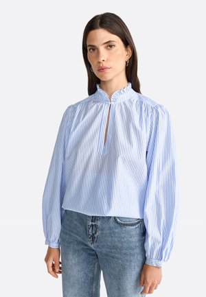 Light blue and white striped blouse with a high neckline, puffed sleeves, and a keyhole opening at the front, paired with denim bottoms.