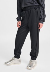 Svarta joggingsbyxor med elastisk midja och sidofickor, tillverkade av ett slätt tyg, tillsammans med silvriga träningsskor med vita detaljer.