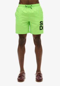 Costumi da bagno verde neon con vita regolabile, logo nero "SUPERDRY" stampato sul lato sinistro e materiale leggero e liscio.