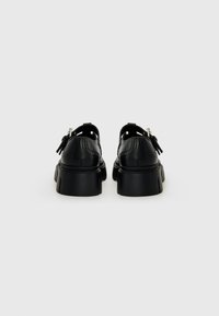 Chaussures en cuir noir avec une semelle épaisse, dotées de perforations et de sangles ajustables. Texture lisse et design robuste.
